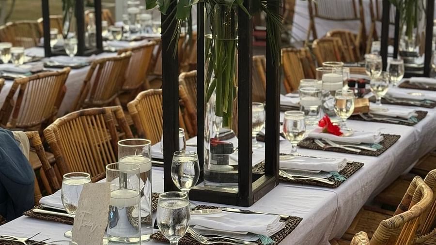 A huge open dining area meant for wedding guests. There are chairs placed with dining tables which features plates, towels, table mat, cutlery, etc. along with flower vases.