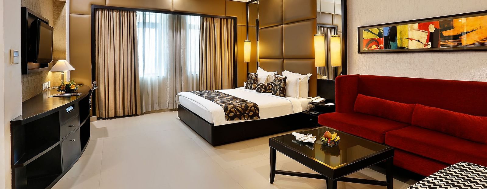 A spacious junior suite with a sleek design, featuring a large bed, red sofa at The Manor, Bareilly
