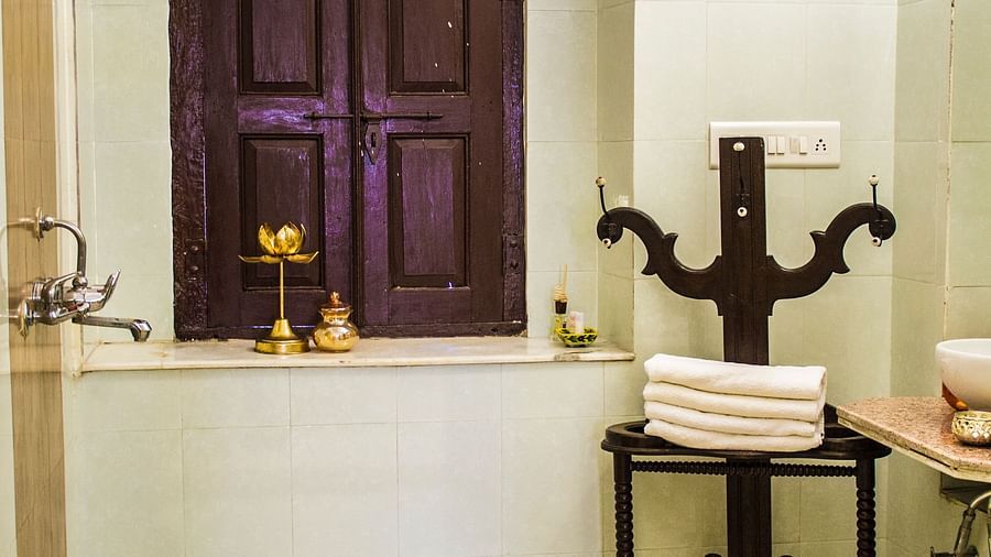 A bathroom with a dark wooden window, a towel rack with folded white towels, and a small golden lamp on the windowsill at Umaid Vilas Jaipur.