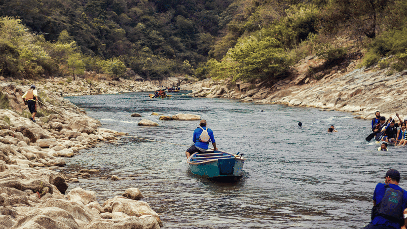 People on a raft moving through a river amidst the mountains on either side.