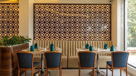 Dining area at Mastiff Grand The Sia Palace Suites & Banquets, Khopoli, with tables set, a banquette, and a large decorative jali screen on the wall.
