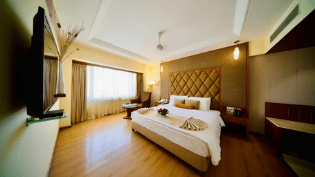 A warmly lit suite in Lords Plaza Ankleshwar with modern interiors featuring a double bed and a large window with its drapes closed