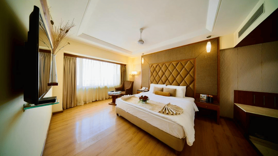 A warmly lit suite in Lords Plaza Ankleshwar with modern interiors featuring a double bed and a large window with its drapes closed