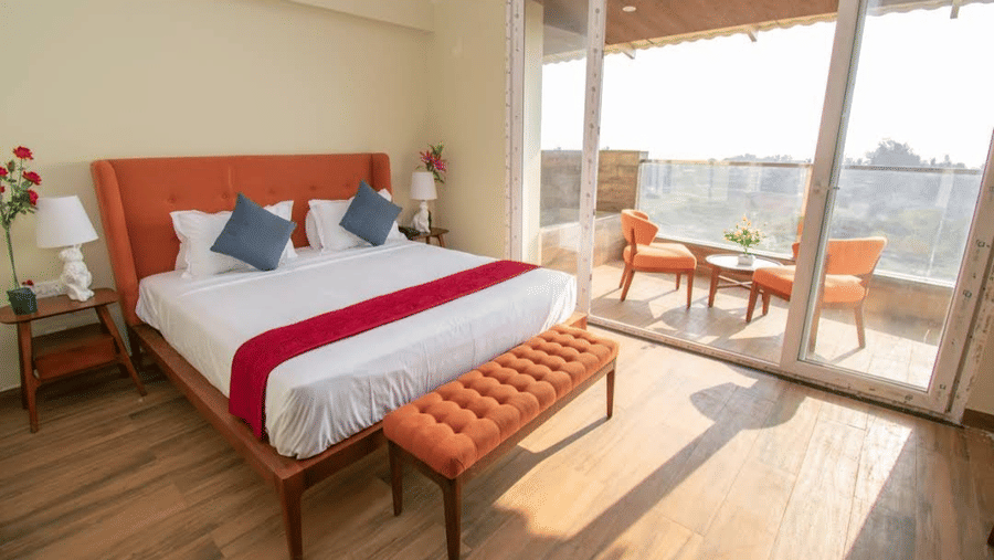 A bedroom featuring an orange headboard, white bed with a red runner, and an orange bench at Estherea Elite, Morjim.