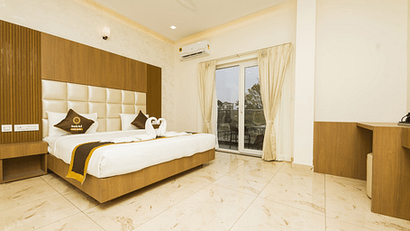 Super Deluxe Room With Balcony featuring a king size bed with a wooden headboard, and decorative pillows, alongside light-coloured walls, tiled flooring.- Sukhi - A Luxury Stay Inn, Chikkamagaluru