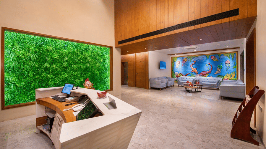 A large, spacious lobby in Lords Inn Jamnagar featuring a reception desk, two large wall paintings, wooden panelling on one side, and sofas for seating.