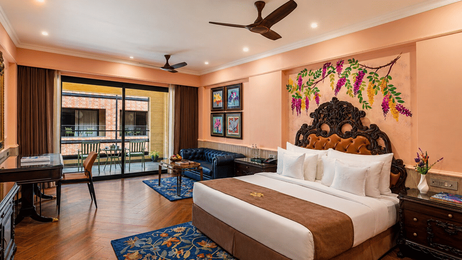 A king size bed, a workspace, and a sofa next to a glass door leading to a balcony in an Executive King Bed Room at MAYFAIR Bay Resort, Paradeep.