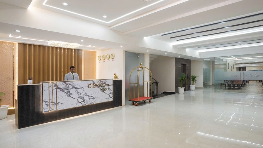 A sleek hotel reception with a marble-patterned front desk, gold accents, and a staff member behind the counter. – Clarks Inn Suites, Near Taj Mahal