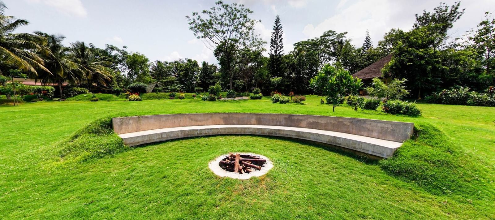 Circular fire pit with curved concrete seating, surrounded by a well-maintained lawn at Fireflies Resorts, Kabini.