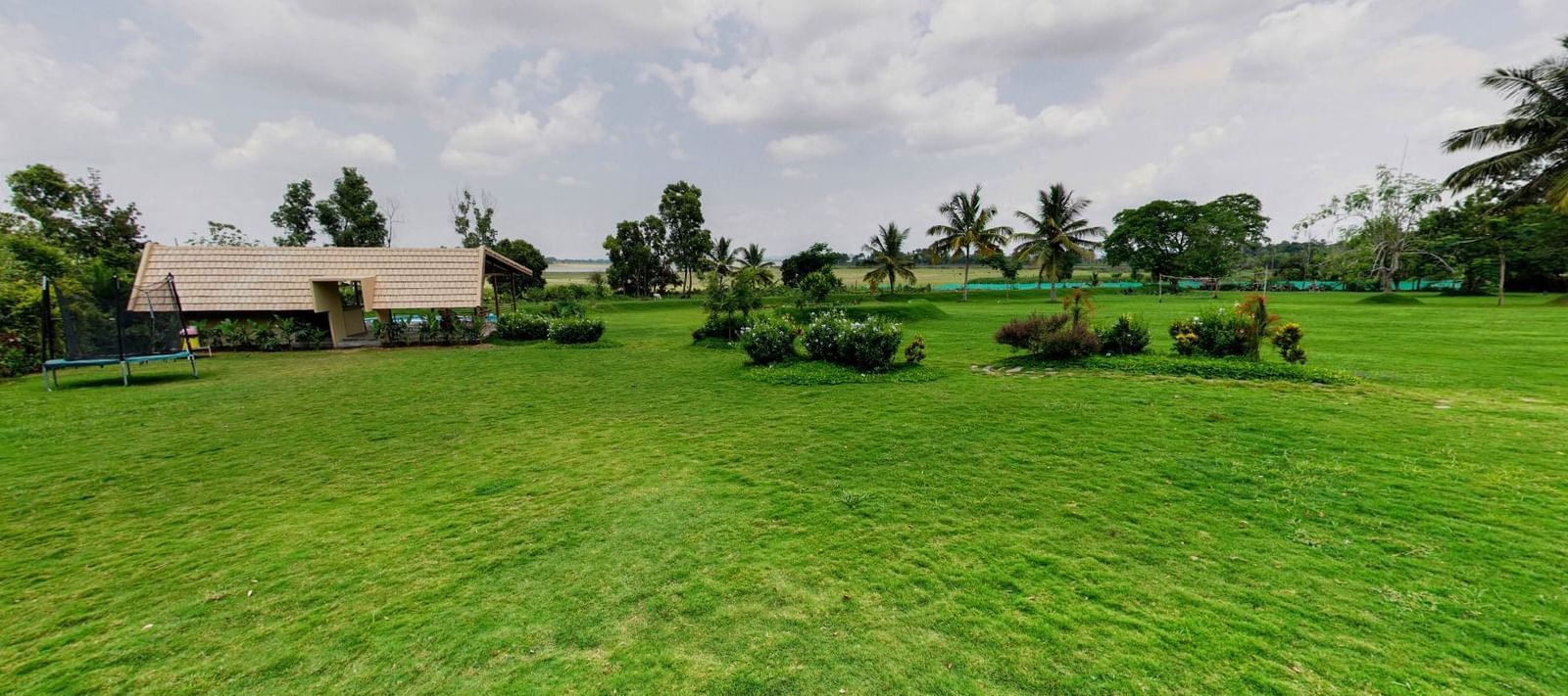 Expansive lawn with trimmed grass, scattered plants, and a single-storey building in the distance at Fireflies Resorts, Kabini.