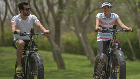 a couple cycling amidst lush green lawns - Karma Lakelands.