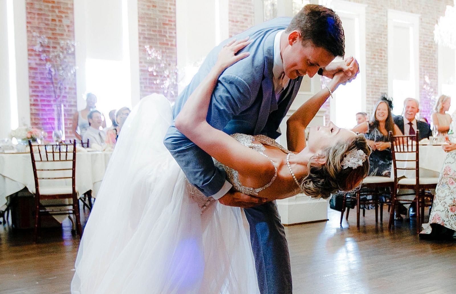 A bride and groom dancing during wedding celebration with people sitting behind the tables in the background. 