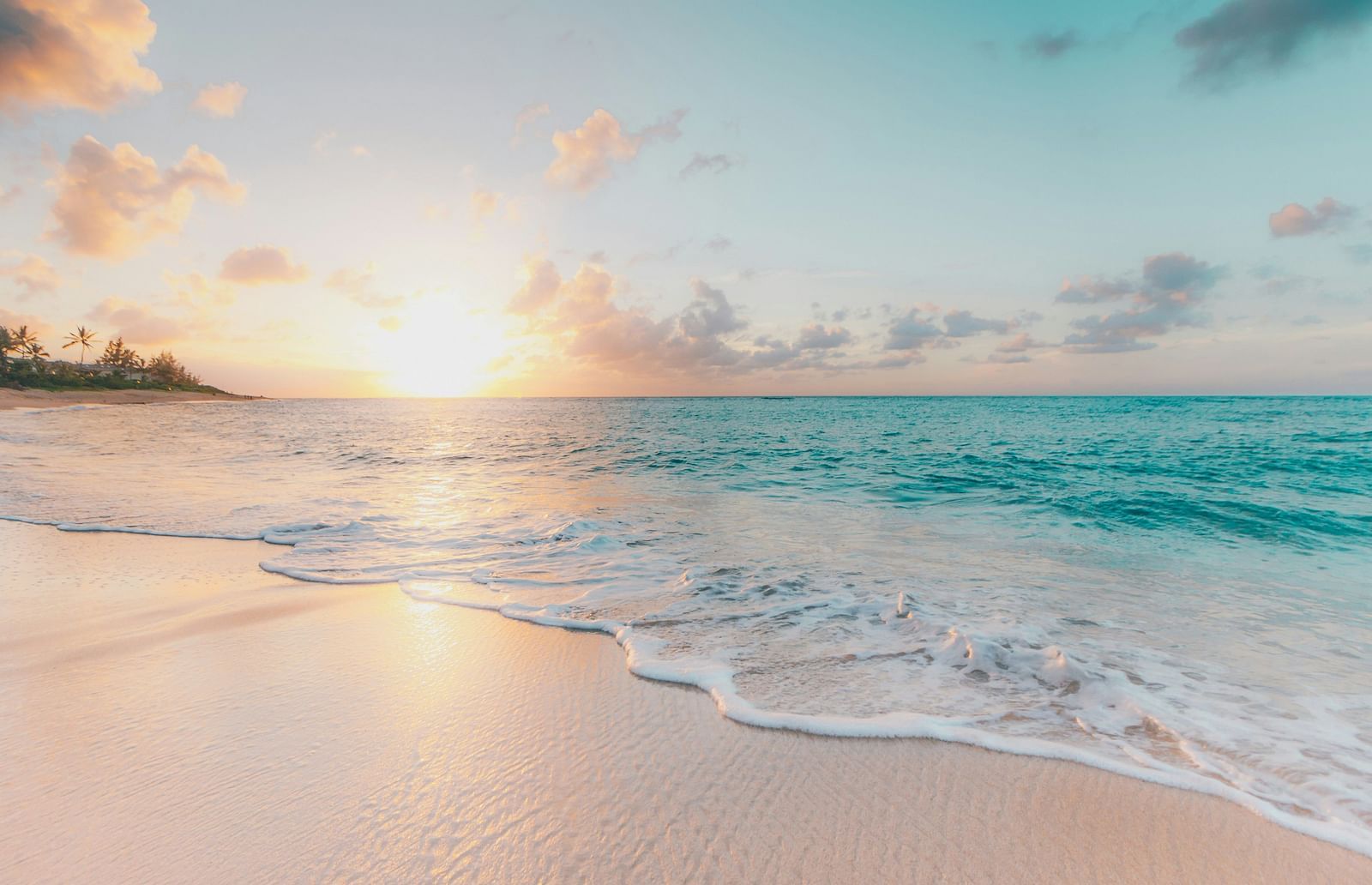 Tranquil beach scene at sunrise with soft pastel hues on the sky.