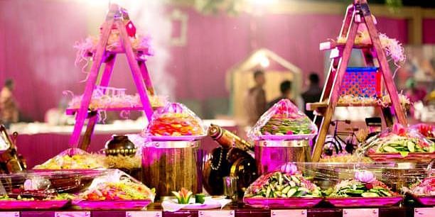 Lavish wedding offerings and decorations arranged on a pink-lit stage for a traditional Indian ceremony.