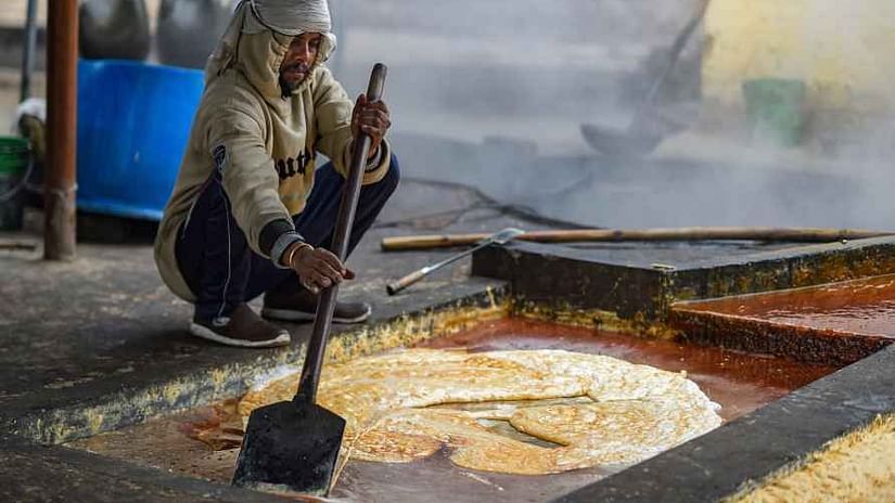 A person stirring a large vat of steaming liquid during the process of making jaggery, with steam rising and the person using a paddle - Black Thunder, Coimbatore