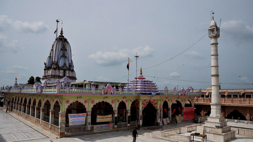 The Tijara Jain Temple in Alwar, Rajasthan, showcases its intricate architecture with a towering shikhara, arched walkways under a cloudy sky.