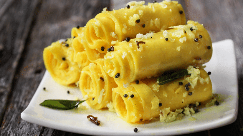 A side view of khandvi elegantly served on a plate, garnished with grated coconut, mustard seeds, and aromatic curry leaves.