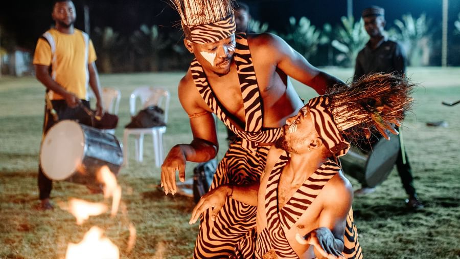 Two people wearing traditional tiger-print outfits and performing while by standers watch -Daksh Eden Greenz, Sasan Gir