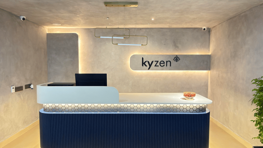 Modern hotel reception desk with the Kyzen logo, warm ambient lighting, textured walls, and a contemporary navy and white counter.