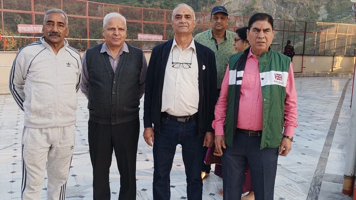 A group of five people standing barefoot on a platform, with mountains in the background. They are dressed in casual clothing and smiling for the photo.