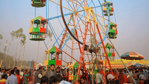 A carnival  showing the close-up of a ferris wheel showing its structure and passenger cars with people around it.