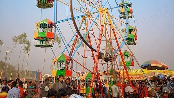 A carnival  showing the close-up of a ferris wheel showing its structure and passenger cars with people around it.