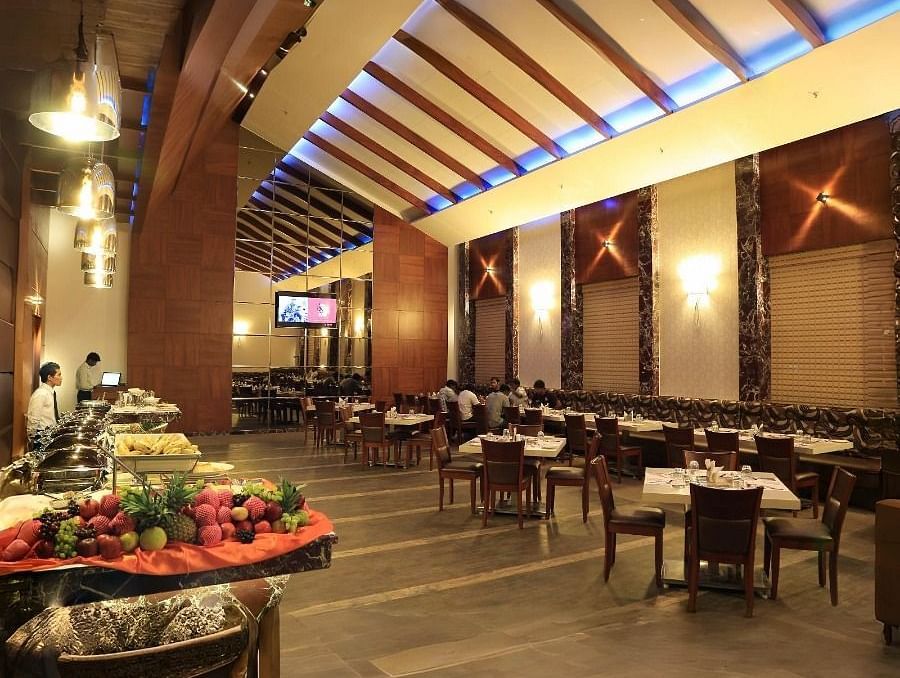 The interior of the Aroma restaurant in Dhanalakshmi Srinivasan Hotels, Perambalur, showing a buffet spread, dining tables, and chairs. The restaurant features wooden ceiling beams and tiled flooring.