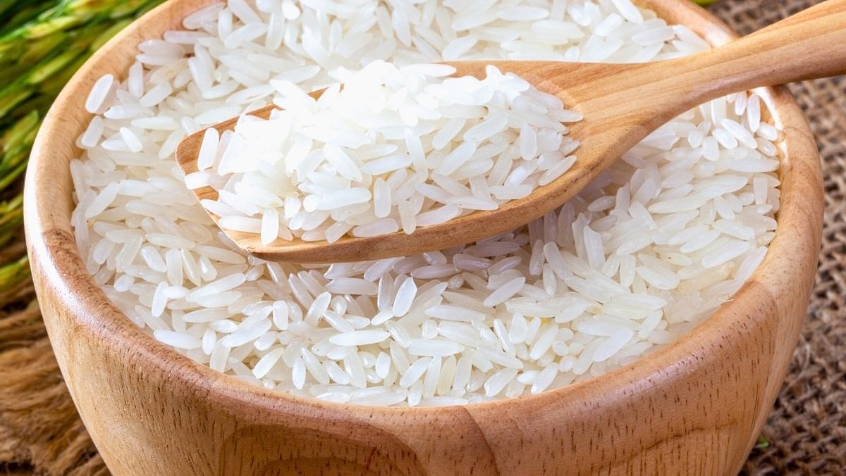 A wooden bowl filled with white jasmine rice placed on green grass, with a wooden scoop resting on top.