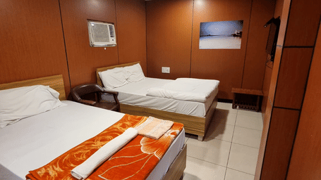 Spacious interior of a Standard 3 Bed Room with 2 beds, tiled floor and an A/C unit at Dream Vision Guest House, Diu.