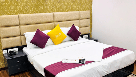 Bedroom of Lime Tree Hotels & Service Apartment Private Limited featuring a padded headboard, pink and yellow cushions, and a patterned rug.