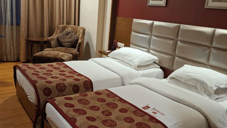 A Deluxe Twin Room at Lords Plaza Surat with 2 single beds, bedside lamps, wooden flooring, a work desk, and a seating area.