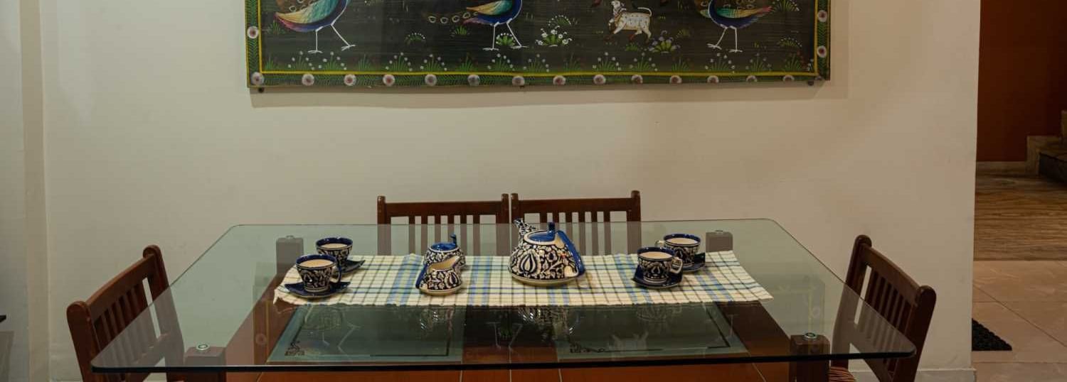 Dining table set with cutlery and wall art, creating a homely indoor dining space for guests at Jaypore360 Homestay.