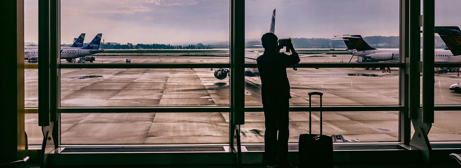 Silhouette of a person standing by a large window overlooking an airport runway.