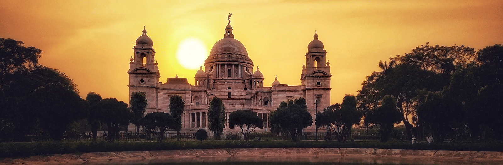 Victoria Memorial in Kolkata at sunset, its marble domes reflected in a pond in the gardens