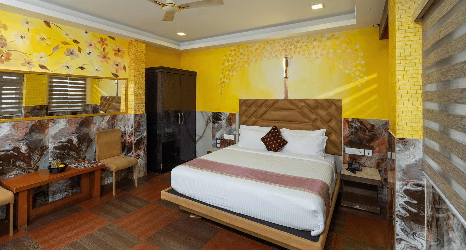 A wide interior view of the Deluxe Non-AC Room at Parakkat Nature Hotel and Resorts, Munnar is featuring a large bed with minimal bedding, patterned walls, dark reflective panelling, and a unique textured floor.