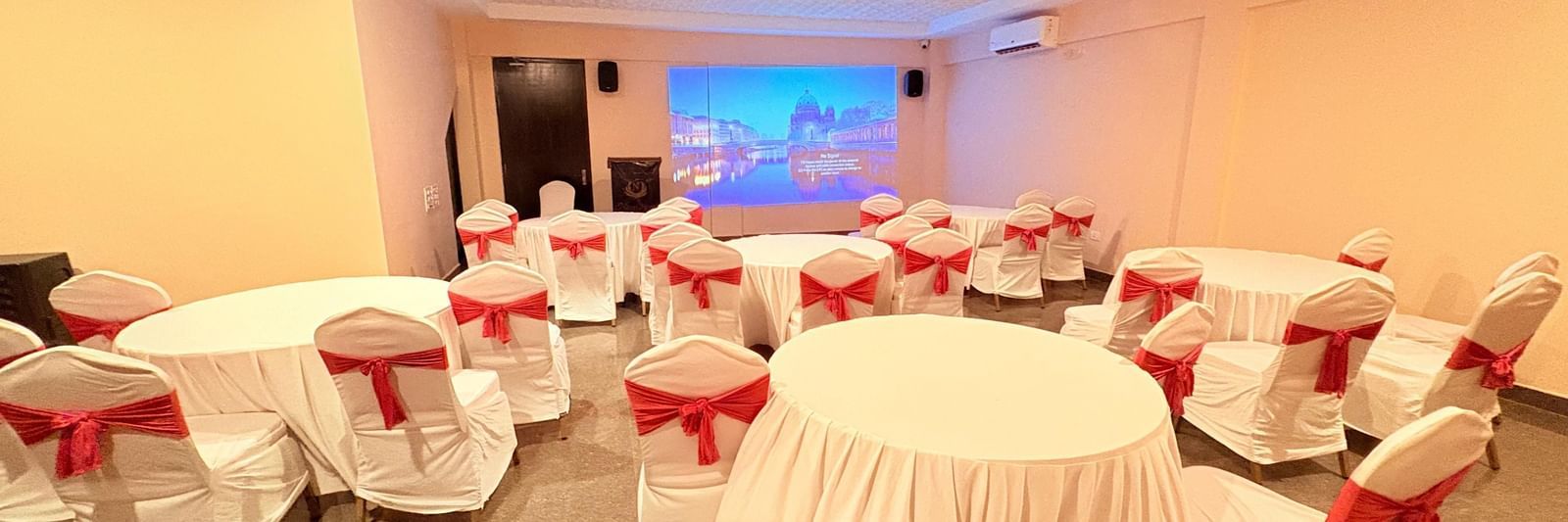 A well-lit conference hall with round tables and red chairs, ideal for meetings and events at Nazri The Verda, Arambol.