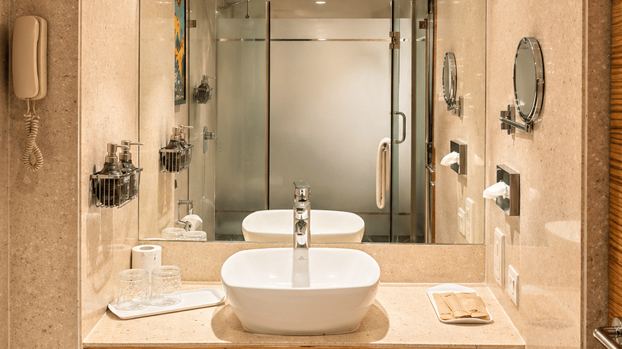 Bathroom with twin sinks, large mirror, and bright overhead lighting at Pride Plaza Ahmedabad.