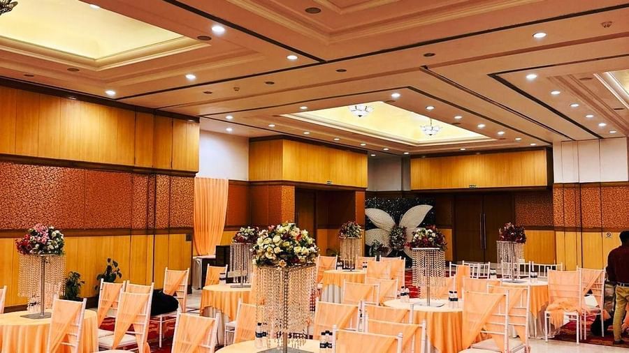 A banquet hall with a patterned carpet, set up with multiple round tables covered with table cloths and chairs.