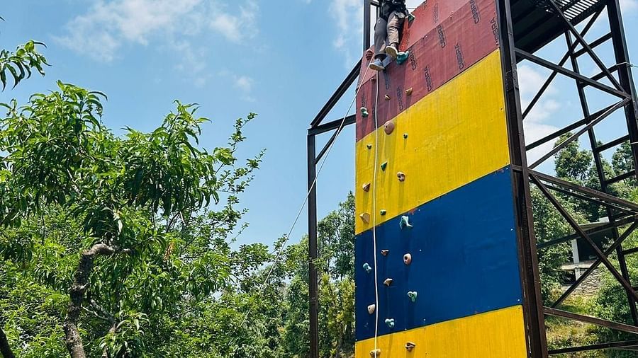 A wider view of the climbing wall against a backdrop of lush greenery and a clear sky, highlighting outdoor activities - Digantaa Resort in Mukteshwar