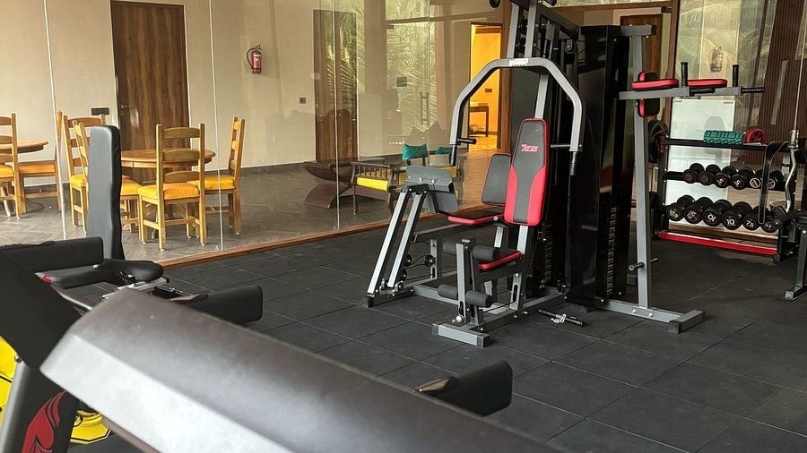A gym interior with a treadmill in the foreground and various strength training equipment, including a multi-gym station, visible in the background; the space features glass walls and a seating area outside the workout zone - Silver Sand Beach Resort, Have