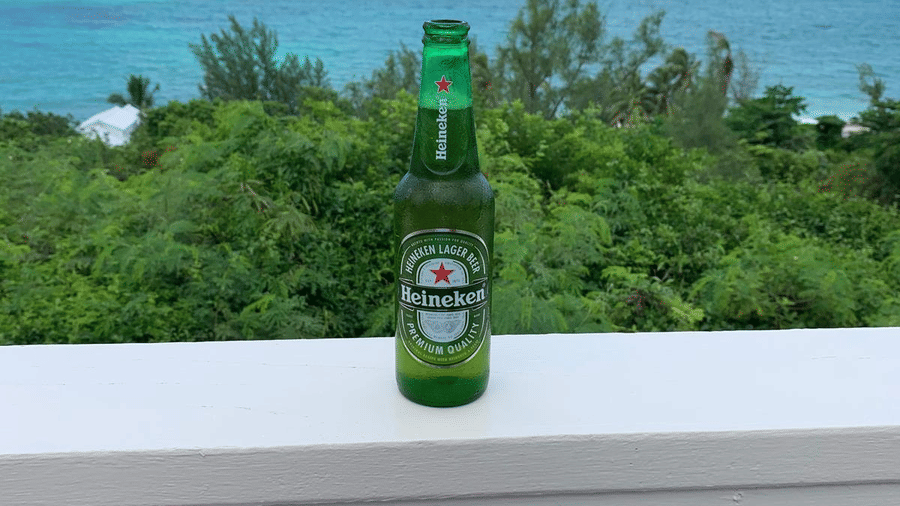 A green bottle placed on a white railing with ocean and trees in the background