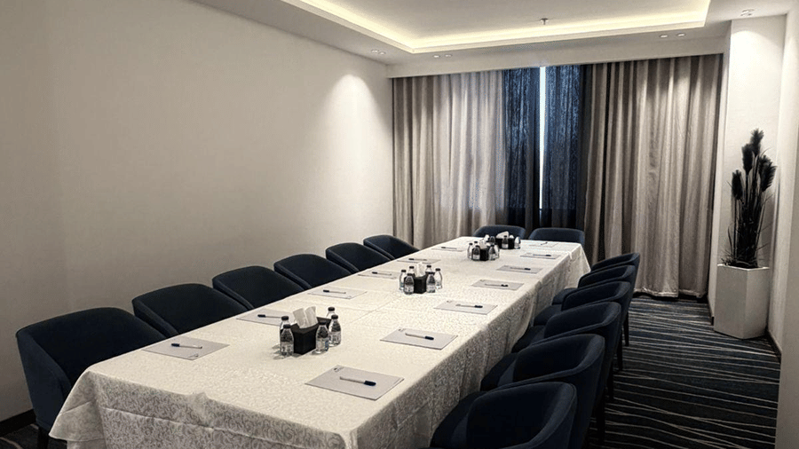 A boardroom at Grand Iva Hotel, Abha featuring a long conference table, padded armchairs, place settings, and ceiling lights. 