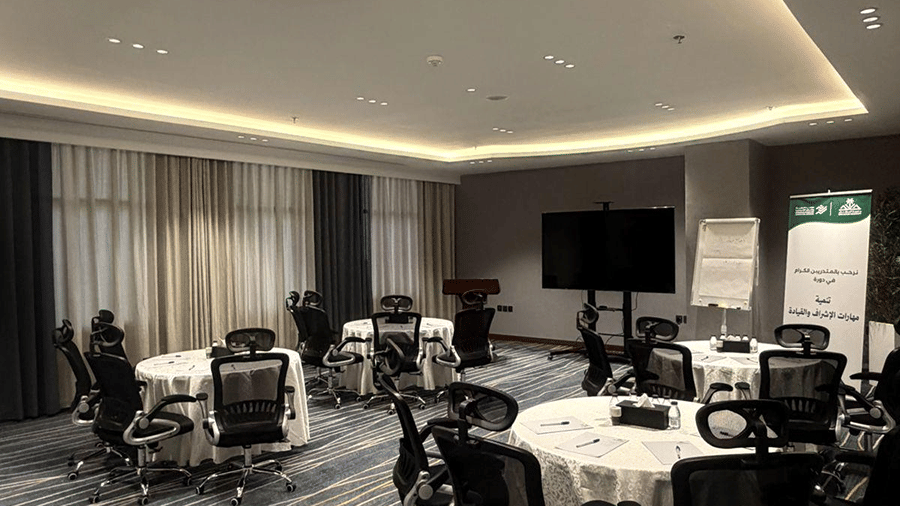 An event hall at Grand Iva Hotel, Abha featuring round seating tables, rolling desk chairs, display monitors, and a white board. 