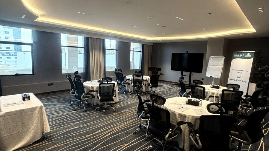 An event space at Grand Iva Hotel, Abha featuring covered round tables, office chairs, display screens, and a side table.