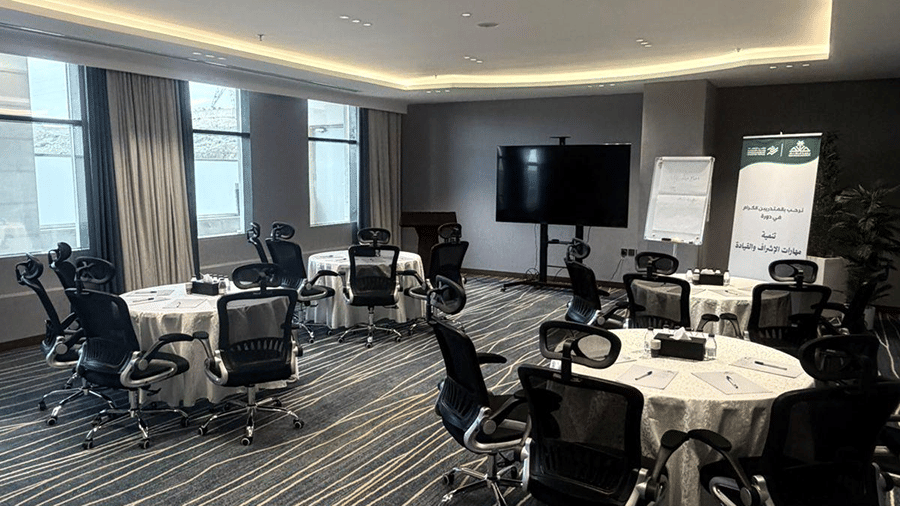 A meeting room at Grand Iva Hotel, Abha featuring round tables, office chairs, display screens, and patterned carpeting.