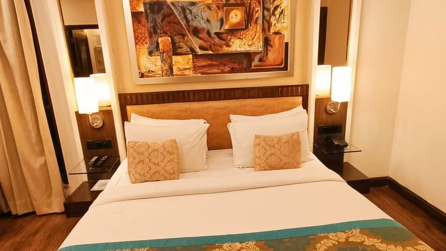Suite with a double bed neatly arranged with plush pillows, bedside tables each topped with a lamp, and a photo frame on the headboard at Inde Signature Tower, Gurgaon
