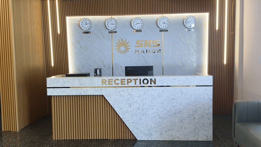 Modern hotel reception desk with a backlit feature wall, wooden counter and polished stone flooring.