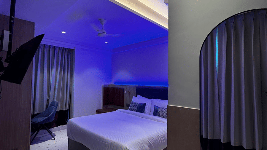 A stylish hotel bedroom featuring a large bed, minimalist decor, and cool blue recessed ceiling lights at Indie Stays, NESCO Goregaon.