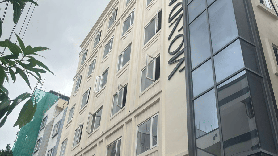  Contemporary exterior view of Monday Premium, Madhapur, showing a multi-storey building with a glass-fronted stairwell and a cream-coloured facade. 