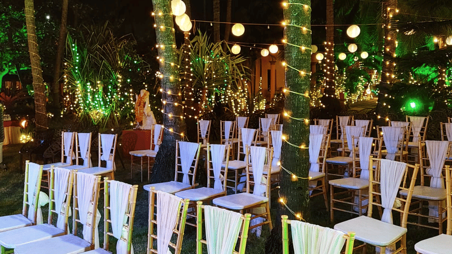 Outdoor wedding seating with white chairs and lights arranged among palm trees at Paradise Lagoon Resort, Udupi.
